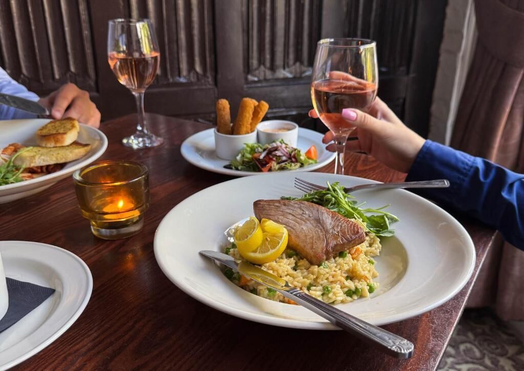 A dining table with plates of food, glasses of wine, and a candle.