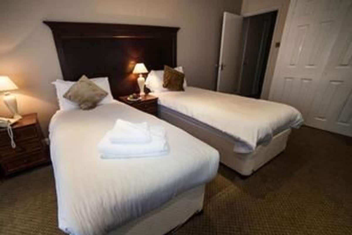 A hotel room with two single beds, a nightstand with a lamp, a dresser, and a door.