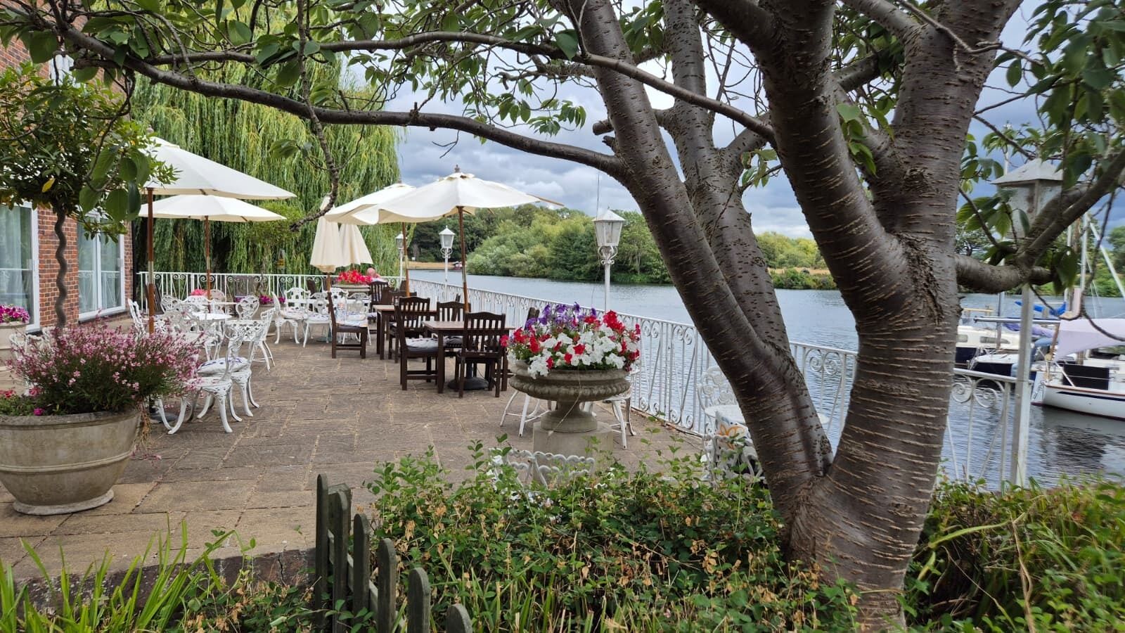 An outdoor patio with tables and chairs, a flower arrangement, and a view of the water.