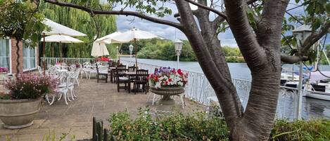 An outdoor patio with tables and chairs, a flower arrangement, and a view of the water.