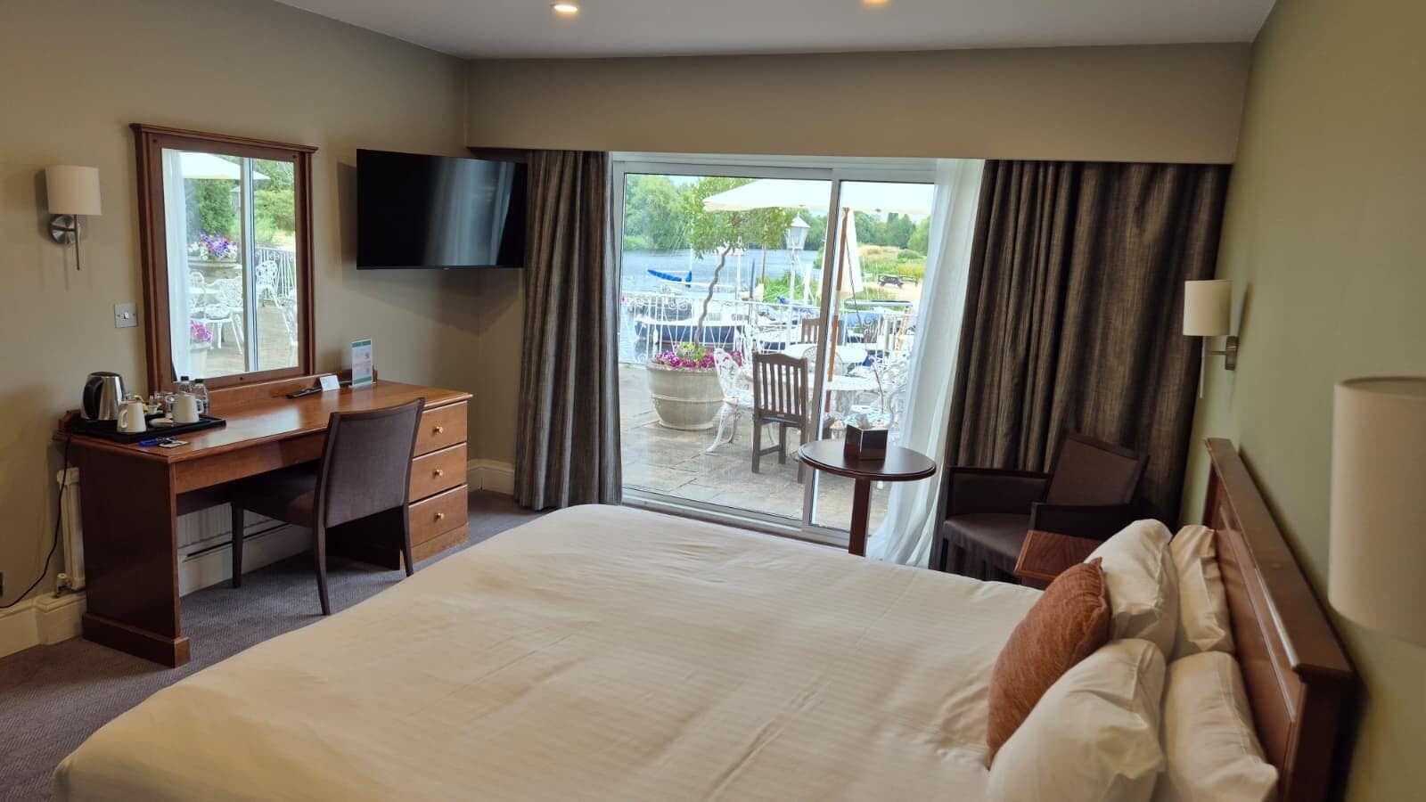 A hotel room with a bed, a desk, a chair, a TV, and a view of the outside.
