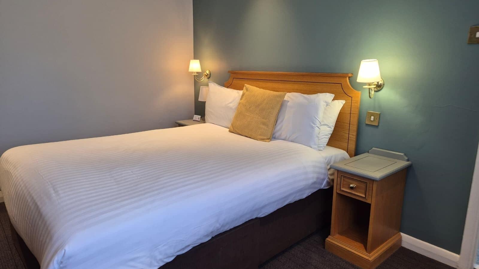 A hotel room with a bed, two bedside lamps, a nightstand, and a wall-mounted light.