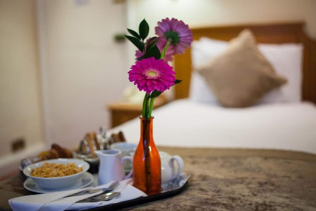 A breakfast tray with a vase of flowers, a bowl of cereal, and a cup of coffee on a table in a hotel room.
