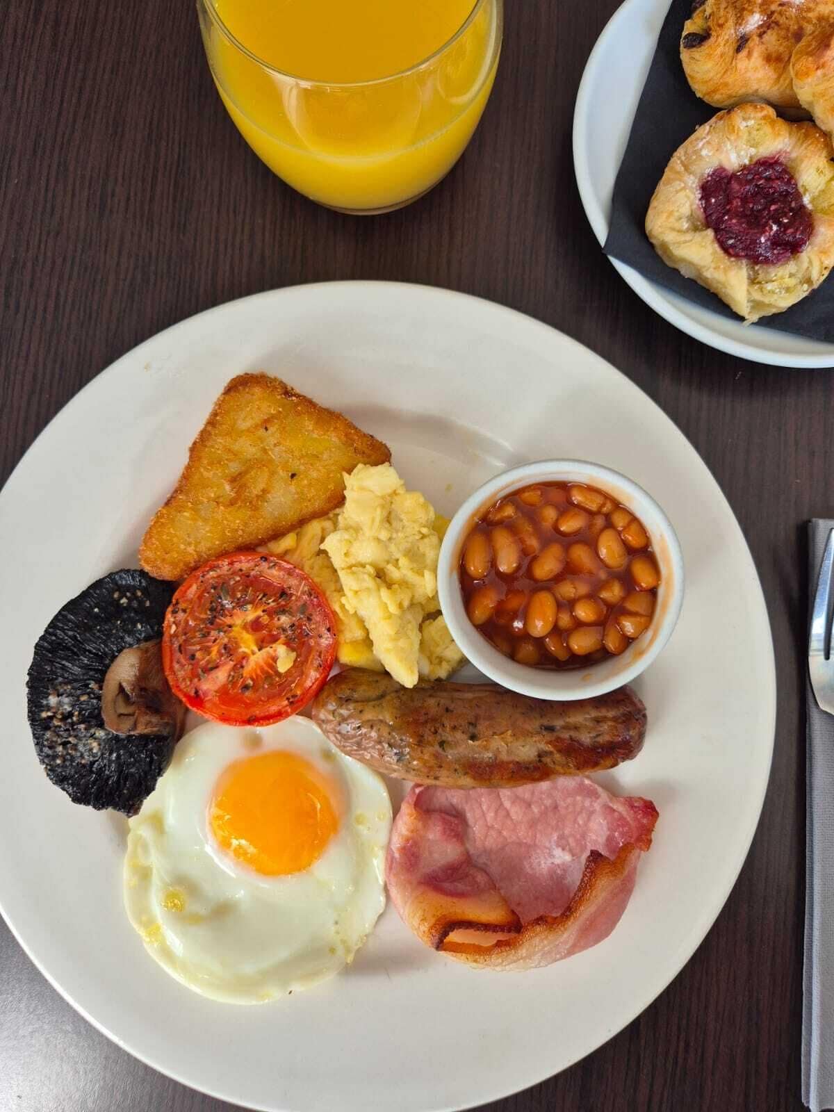 A breakfast plate with toast, eggs, beans, tomatoes, mushrooms, sausages, and bacon.