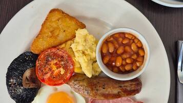 Un plato de desayuno con tostadas, huevos, frijoles, tomates, champiñones, salchichas y tocino.