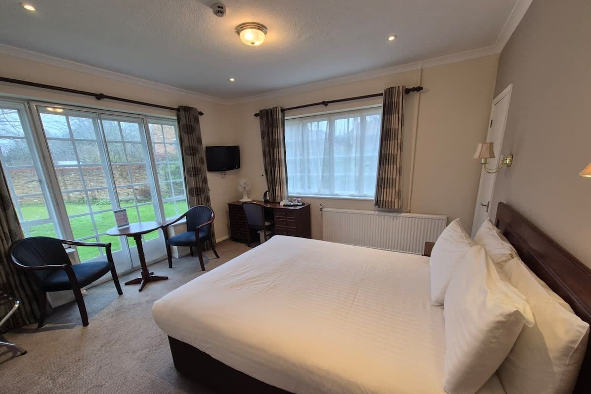 A hotel room with a large bed, a desk with a chair, a television, and a view of the outdoors through large windows.