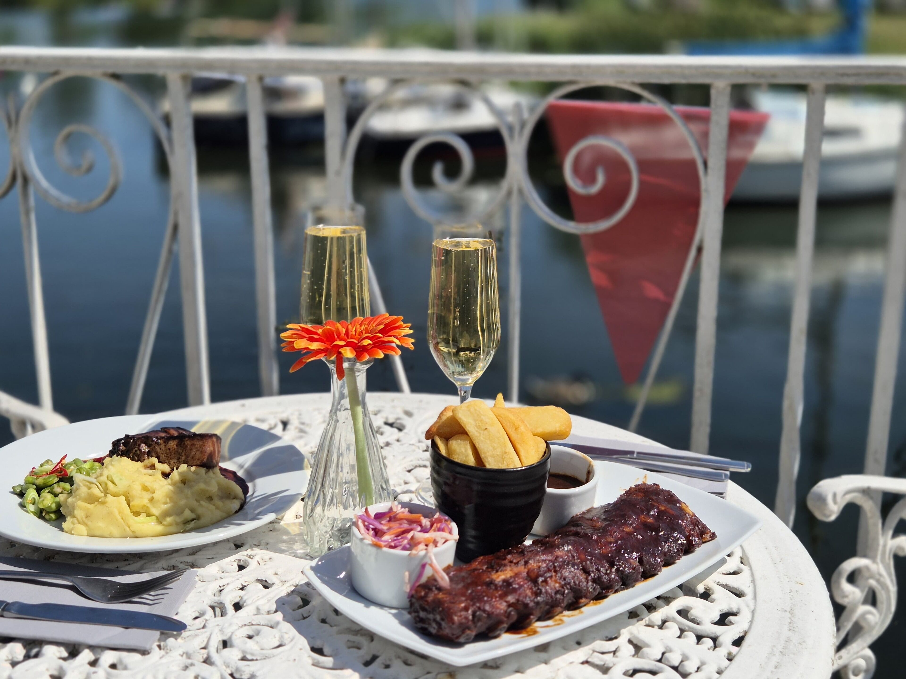 Una mesa con comida y bebidas en un balcón con vista al agua.