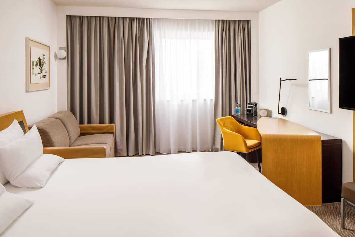 Una camera d'albergo con un letto, una scrivania, una sedia, un televisore e una finestra con tende.