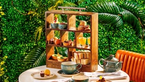 A round table with a wooden dessert display, a teapot, and a chair. - Novotel London Greenwich (London)