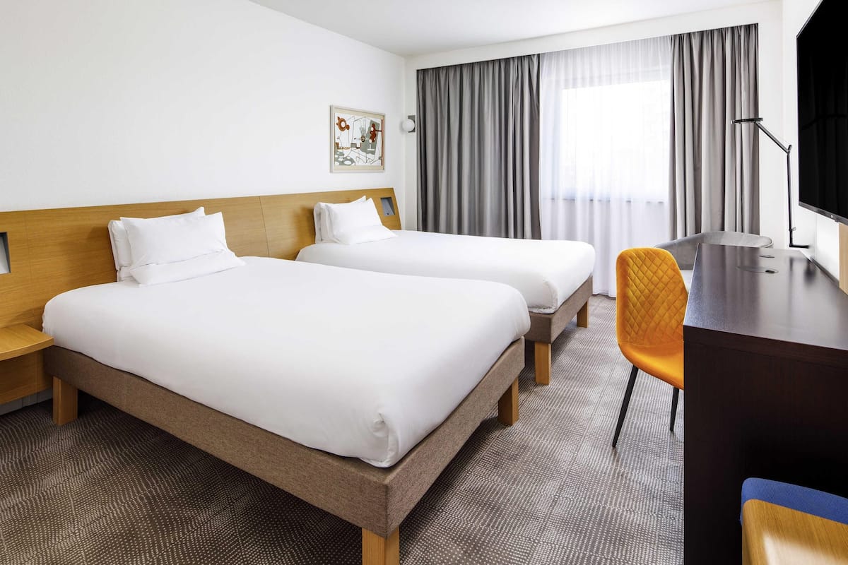 A hotel room with two beds, a desk, a chair, a television, and a window with curtains.