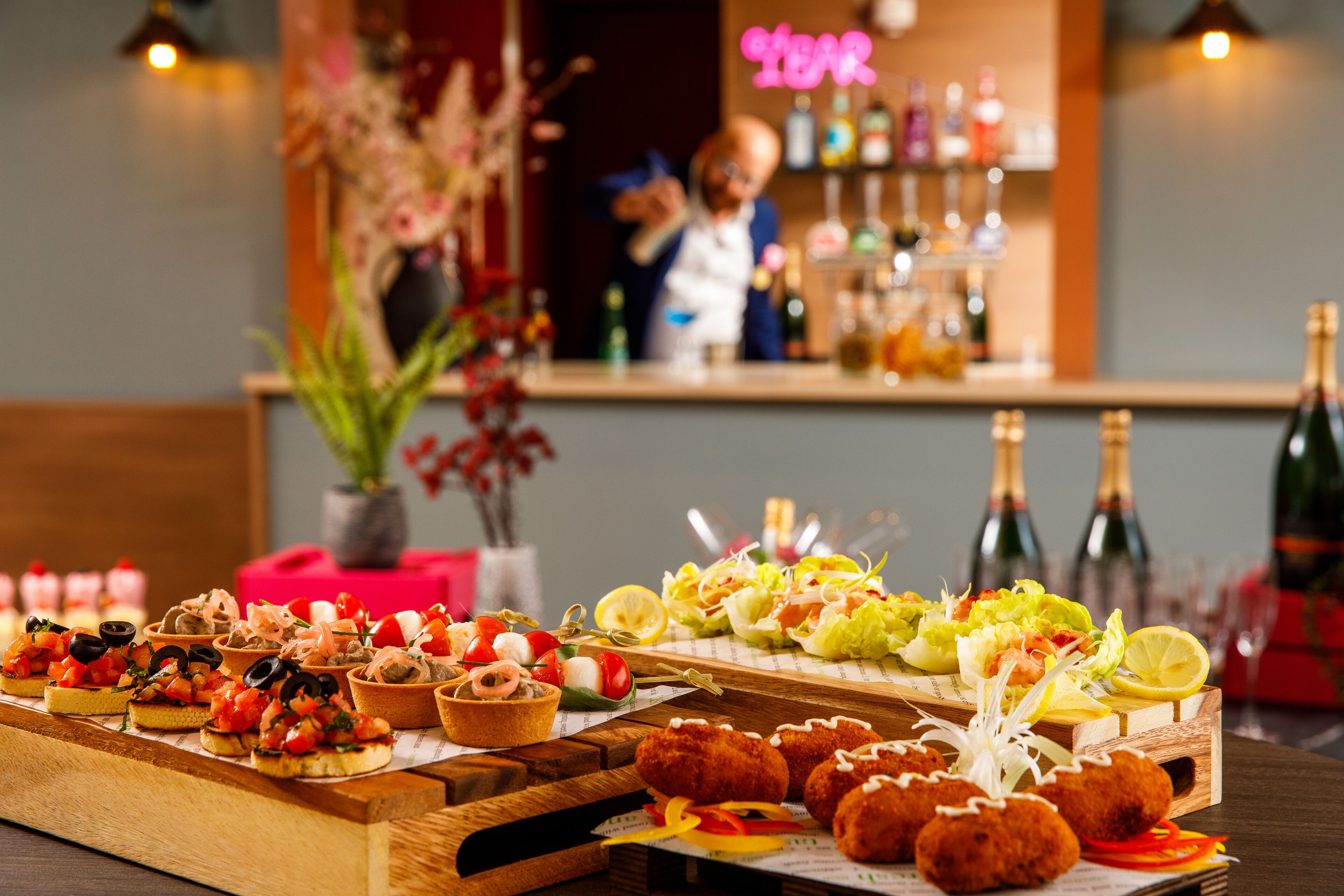A buffet table with various appetizers and a bar area in the background.