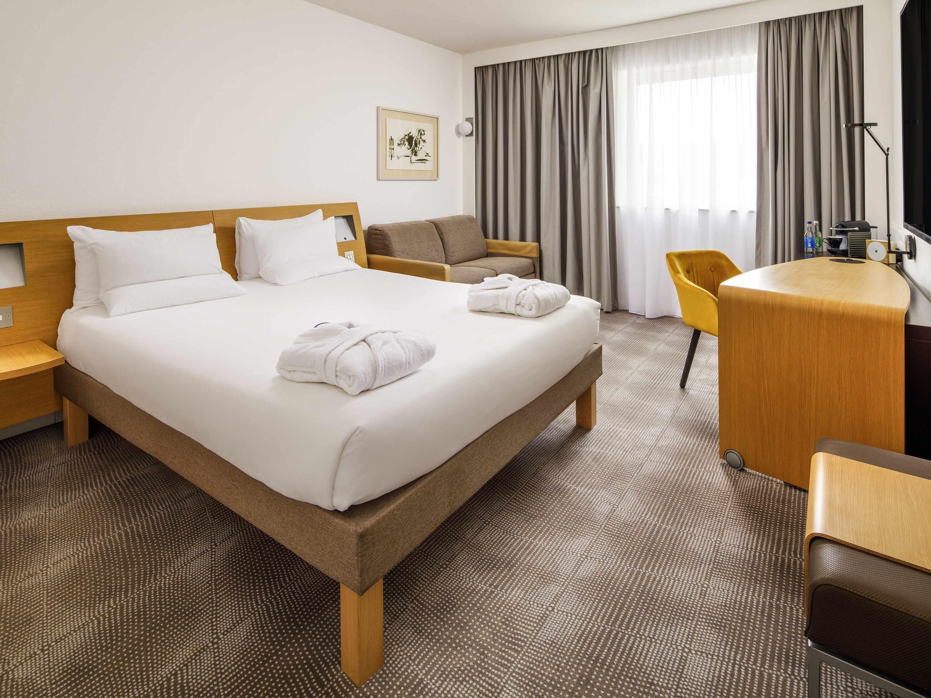 A hotel room with a bed, a desk, a chair, and a television.