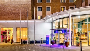 A hotel entrance with a prominent 'NOVOTEL' sign, a glass facade, and a covered walkway leading to the entrance. - Novotel London Greenwich (London)