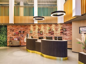 A reception area with a brick wall, wooden slats, and a reception desk. - Novotel London Greenwich (London)