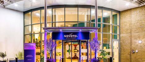 A hotel entrance with a covered walkway, a glass facade, and a sign reading 'NOVOTEL HOTELS & RESORTS.'