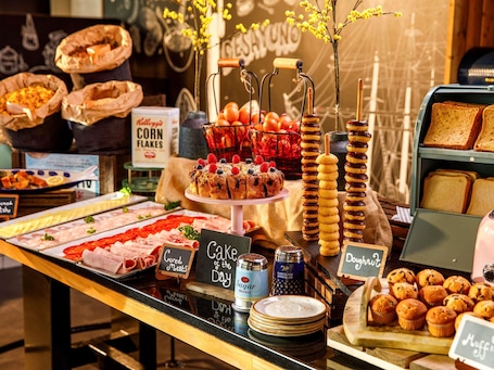 Un buffet proposant une variété d’aliments, notamment de la charcuterie, des gâteaux, des beignets, des muffins et un présentoir de céréales en flocons de maïs.. Novotel London Greenwich
