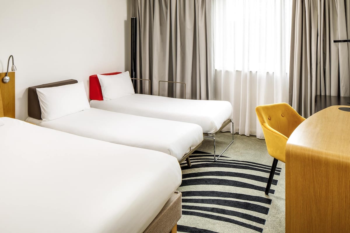 A hotel room with two beds, a desk, a chair, a TV, and a window with curtains.