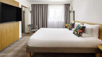 A hotel room with a large bed, a flat-screen TV mounted on the wall, a chair, and a window with curtains.