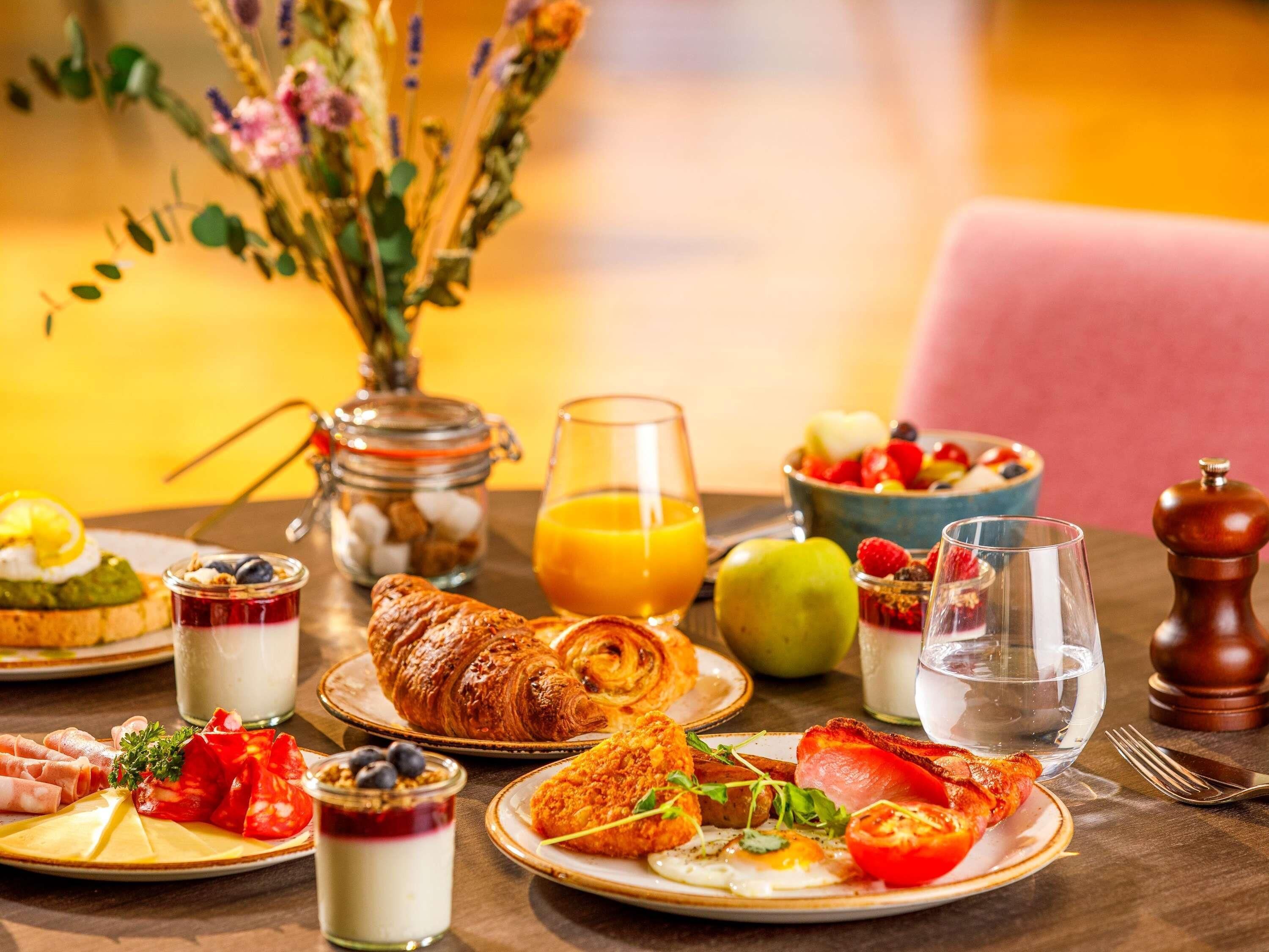 A breakfast table with croissants, eggs, tomatoes, and a bowl of fruit.
