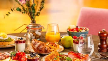 A breakfast table with croissants, eggs, tomatoes, and a bowl of fruit.
