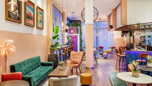 A modern lounge area with a green sofa, a wooden coffee table, and a bar area with stools and a counter. - Novotel London Greenwich (London)