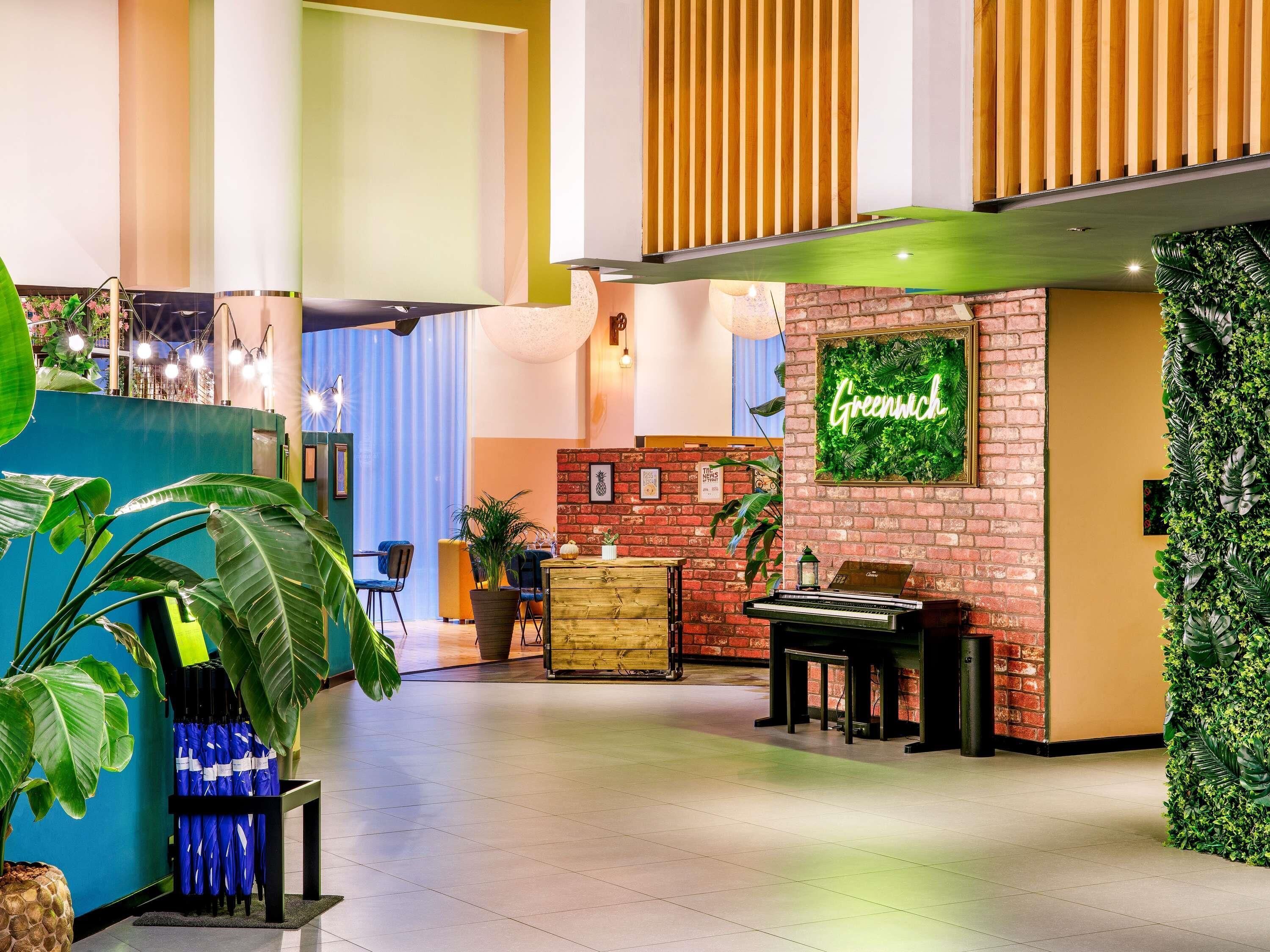 A modern lobby with a green wall, a piano, and a neon sign that reads "Greenwich".