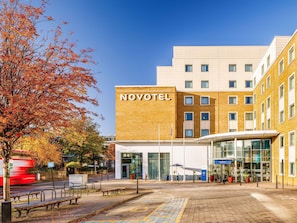 A NOVOTEL hotel with a modern design, a glass entrance, and a paved outdoor area with benches. - Novotel London Greenwich (London)