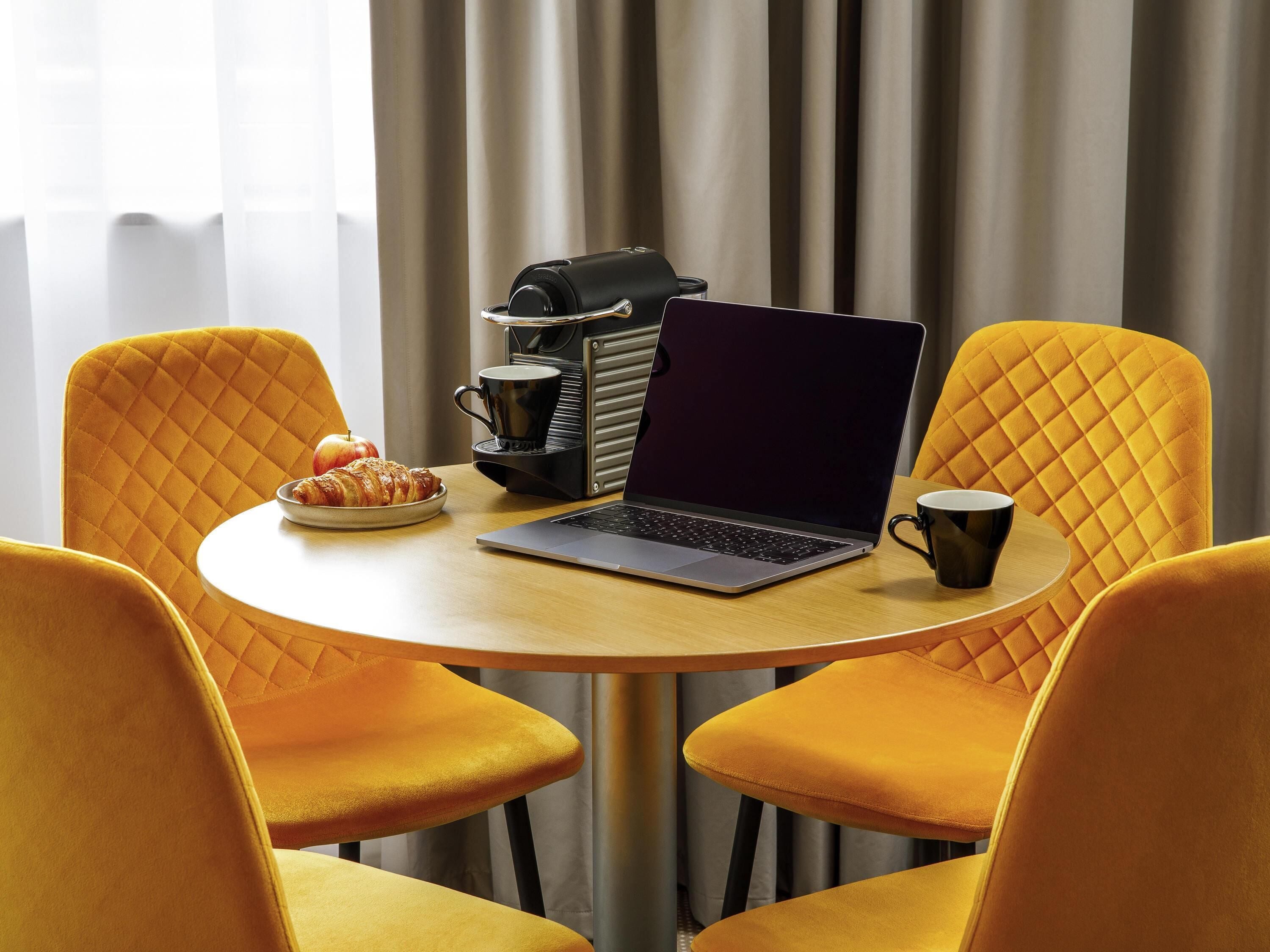 A round table with a laptop, a coffee maker, and a plate with food.