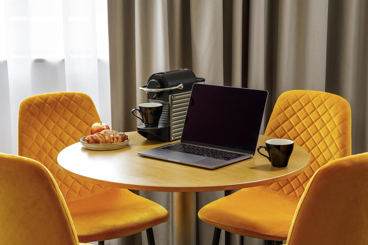 A round table with a laptop, a coffee maker, and a plate with food.