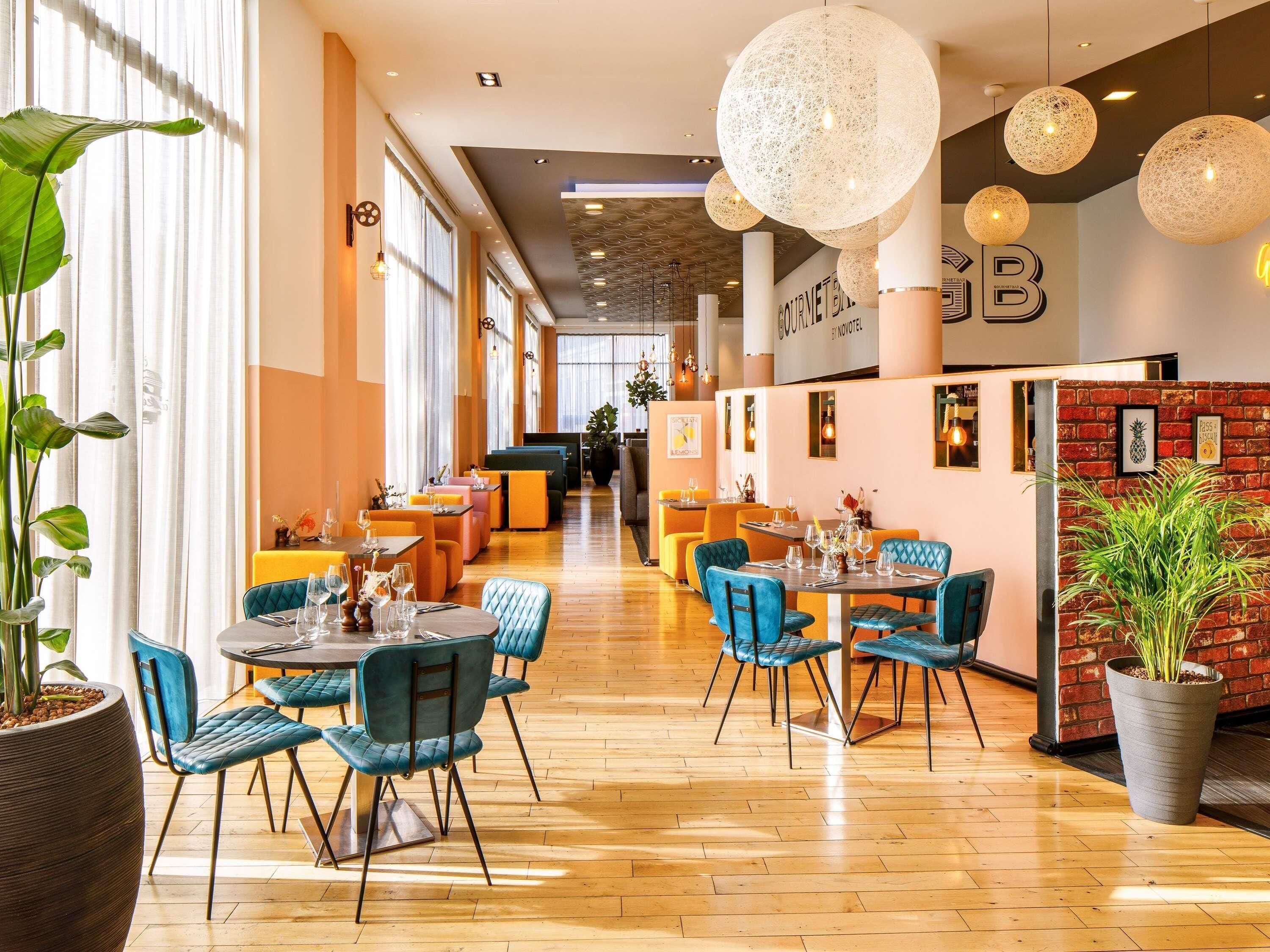 A modern restaurant with wooden flooring, blue upholstered chairs, and hanging spherical light fixtures.