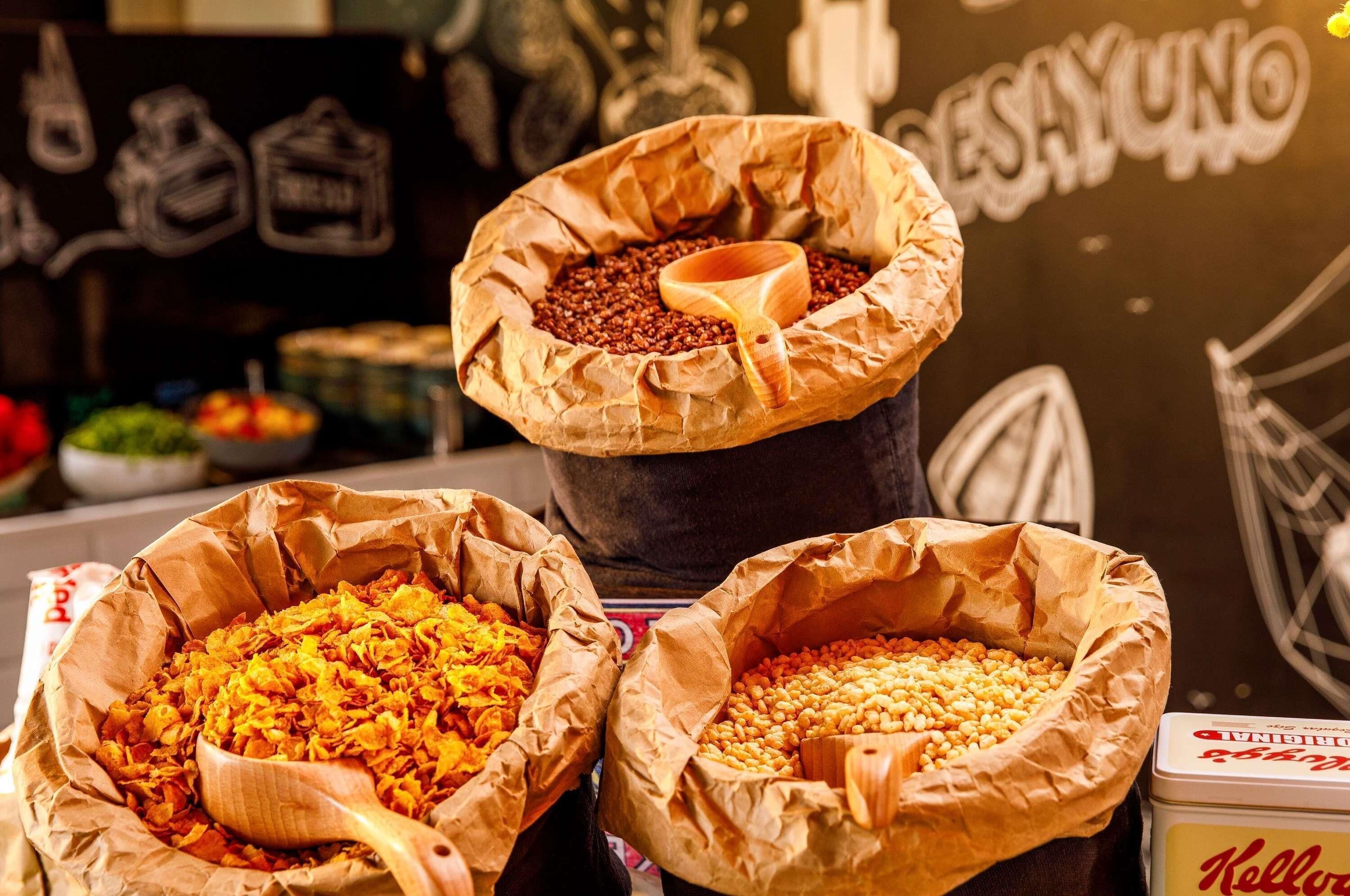 Three large paper bags filled with different types of grains, each with a wooden scoop.