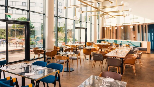 A modern restaurant with large windows, wooden floors, and a variety of seating arrangements including tables and chairs. - Novotel Le Havre Centre Gare (Le Havre)