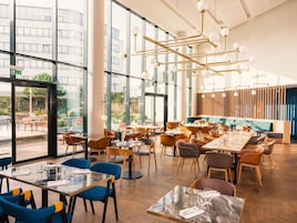 Um restaurante moderno com grandes janelas, piso de madeira e diversos tipos de assentos, incluindo mesas e cadeiras.