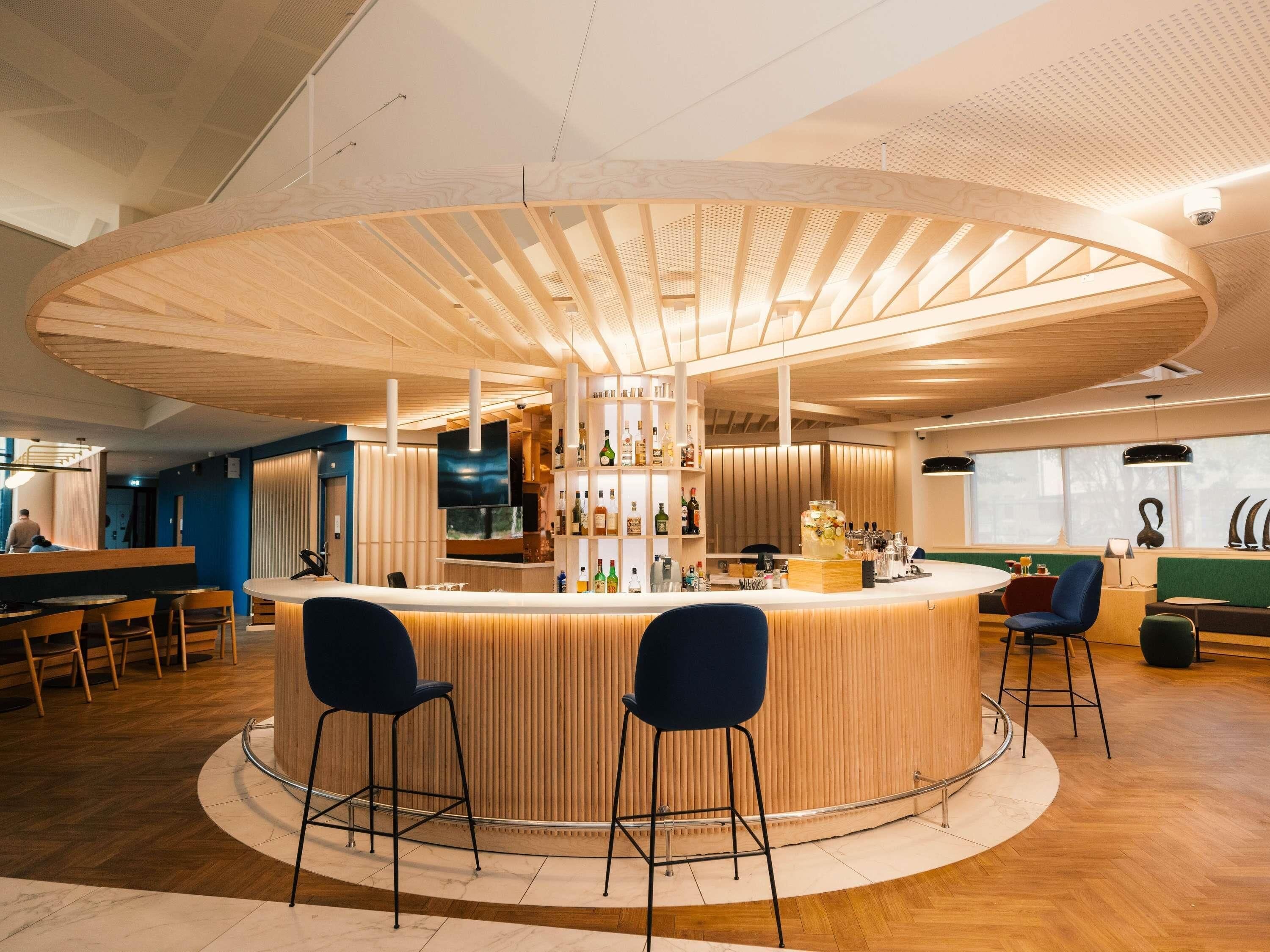 A modern bar area with a circular wooden counter, two bar stools, and a large TV screen.
