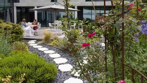 An outdoor seating area with tables and chairs, surrounded by plants and a stone pathway. - Novotel Le Havre Centre Gare (Le Havre)