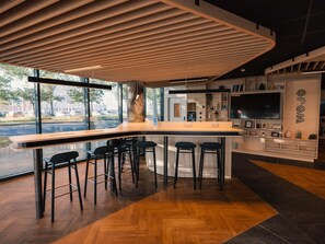 Un espace bar moderne avec un plafond à lattes de bois, des tabourets de bar, un grand téléviseur et une vue sur la rue.