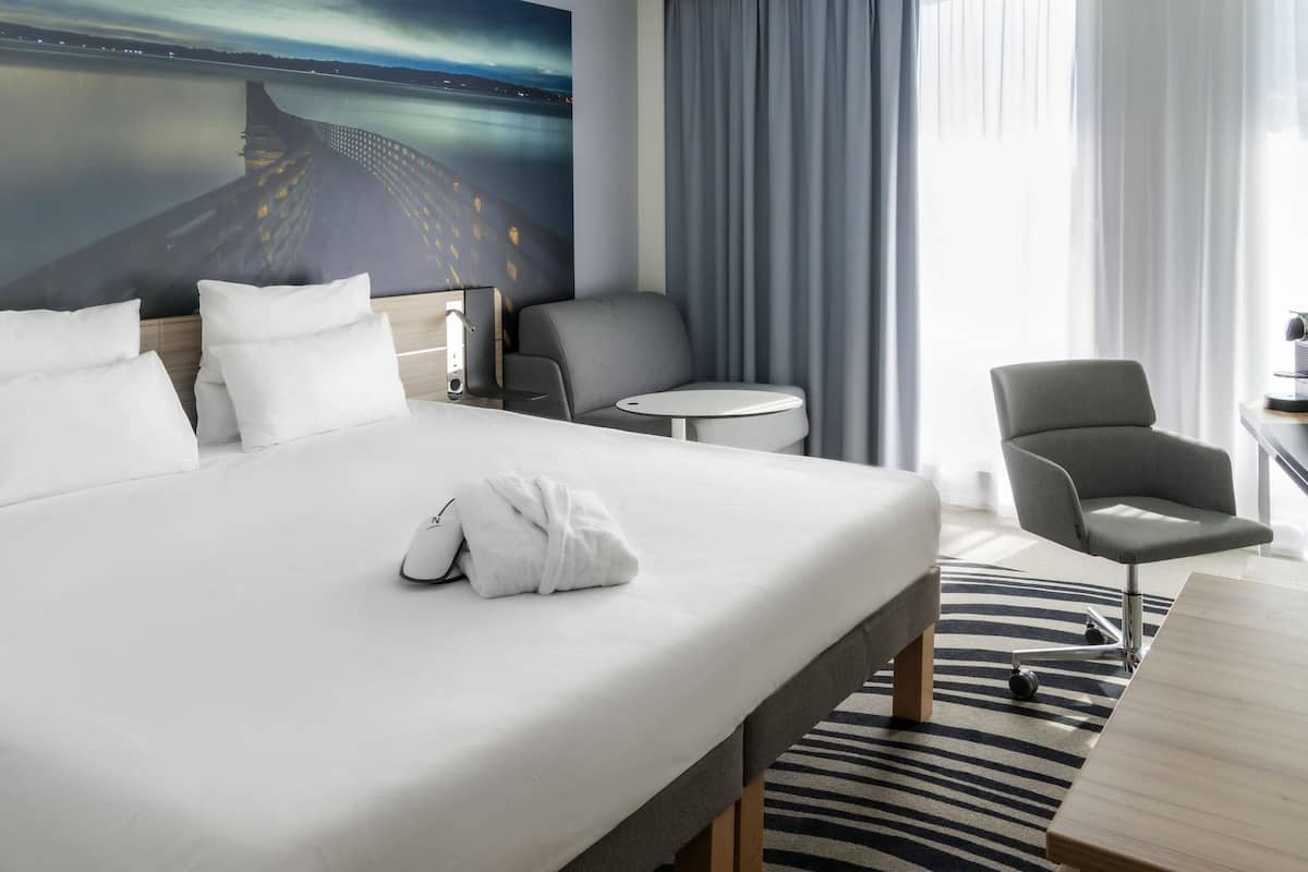 A hotel room with a large bed, a desk, a chair, and a view of a bridge at night.