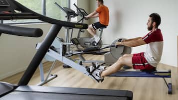 A gym with stationary bikes and treadmills, wooden flooring, and large windows.
