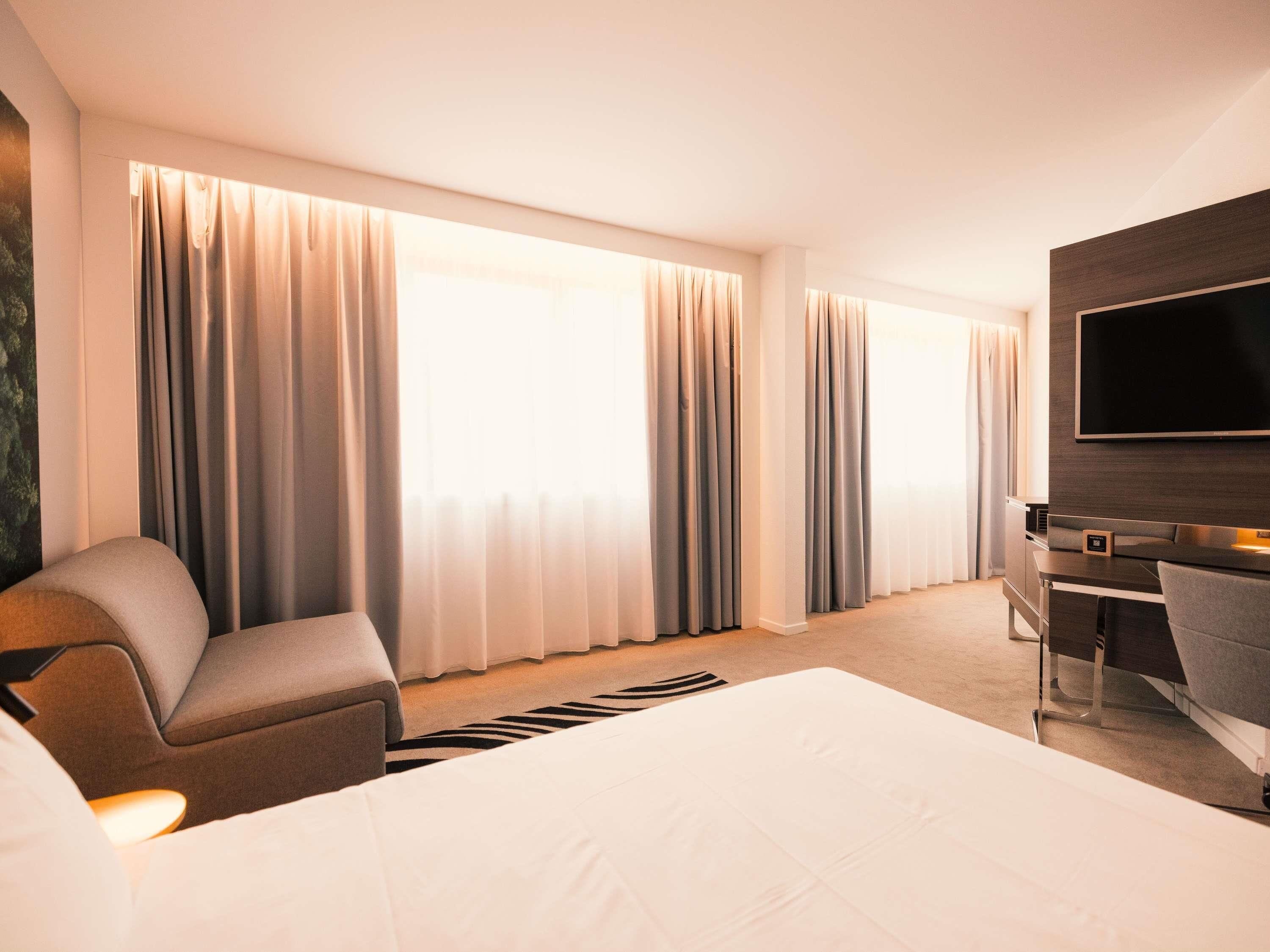 A hotel room with a bed, a desk, a chair, and a TV.