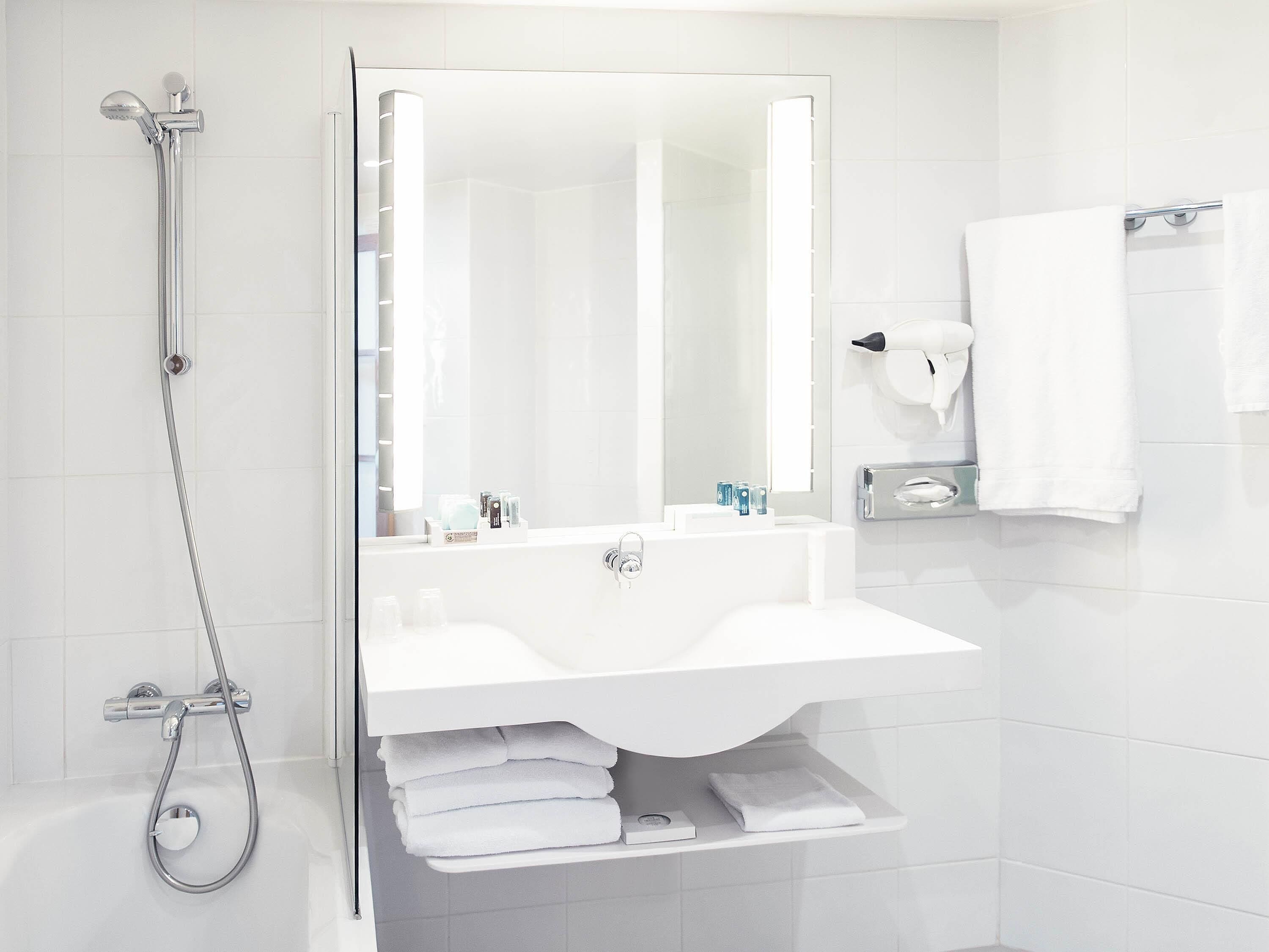 Un baño moderno con ducha de vidrio, lavamanos blanco y un perchero para toallas.