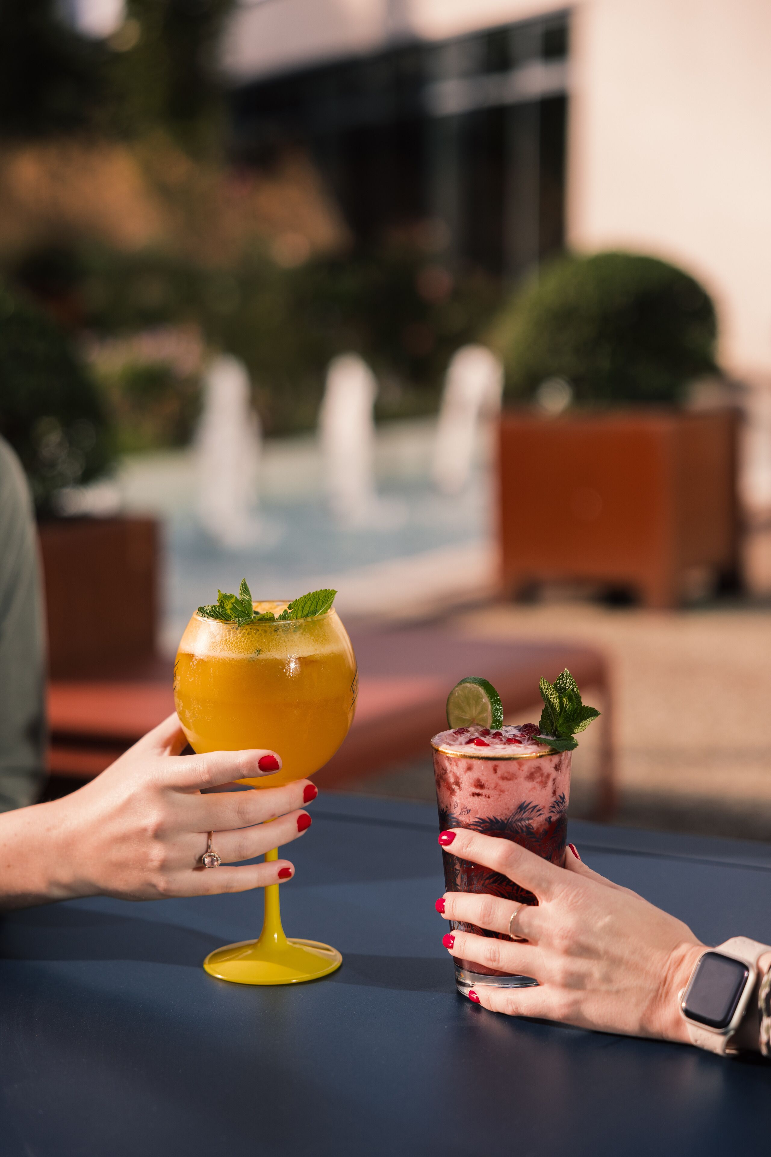 Two people holding drinks at a table by a poolside.