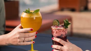 Two people holding drinks at a table by a poolside.
