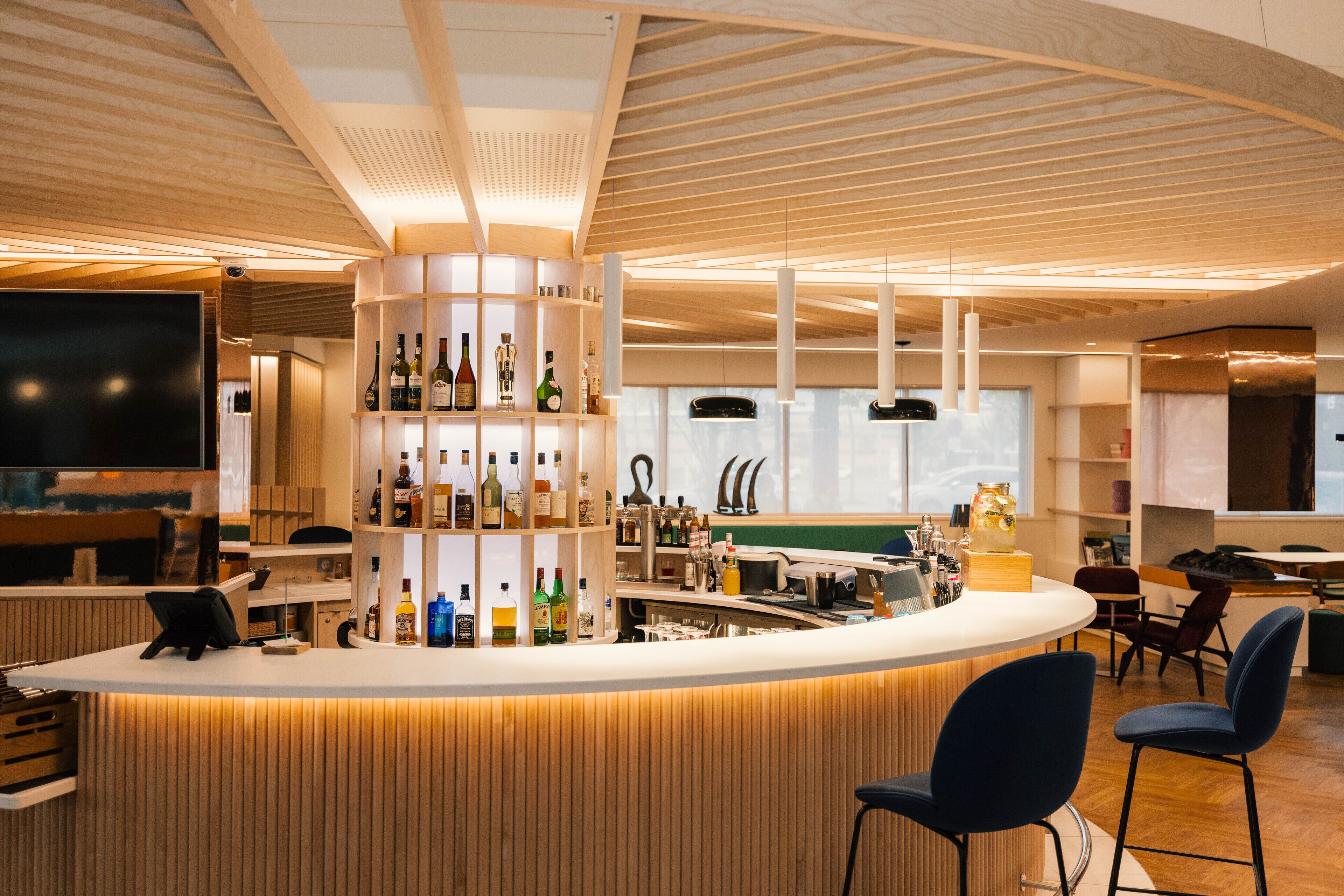 Zona de bar moderna con techo de madera, barra central y asientos.