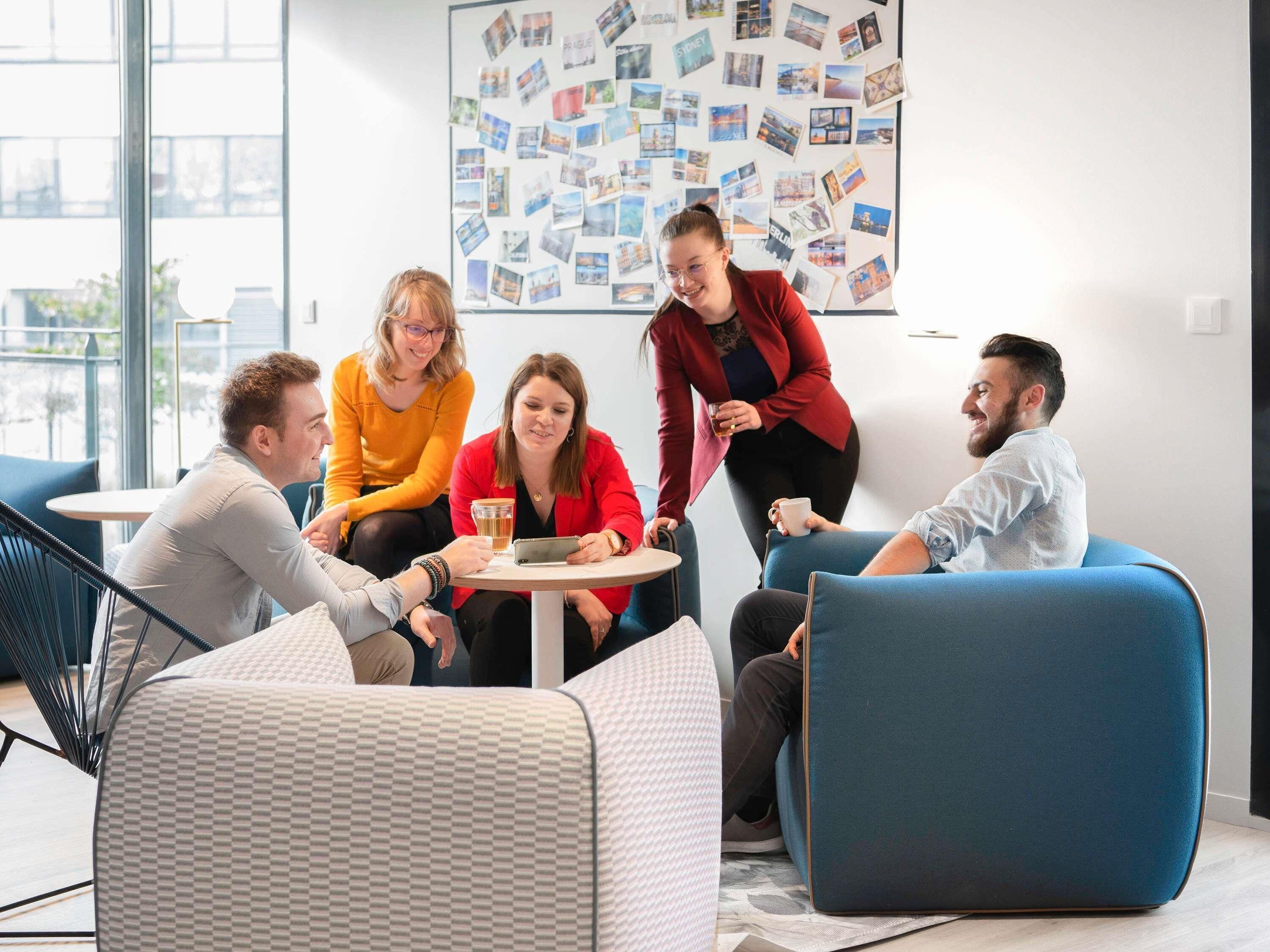 A modern meeting room with a glass wall, a bulletin board with photos, and blue seating.