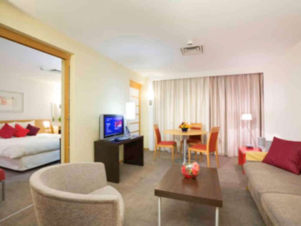A hotel room with a bed, a sofa, a coffee table, a TV, a desk, and a dining area with chairs and a table.