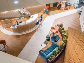 Un vestíbulo moderno con un mostrador de recepción curvo, zonas de estar con sofás y sillones, y un mostrador de madera con una planta.