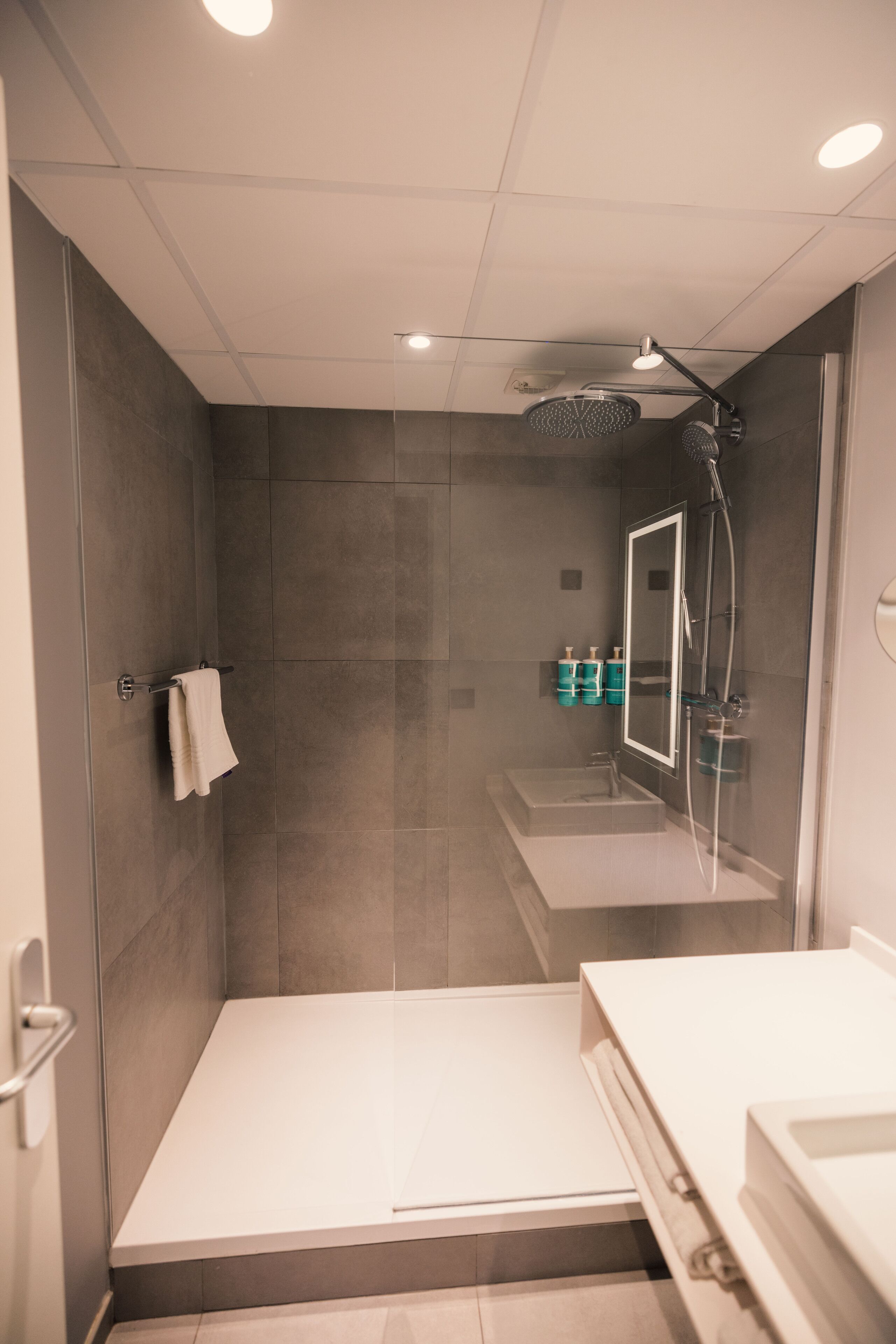 Une salle de bain moderne avec une douche à parois de verre, un lavabo blanc et un miroir.