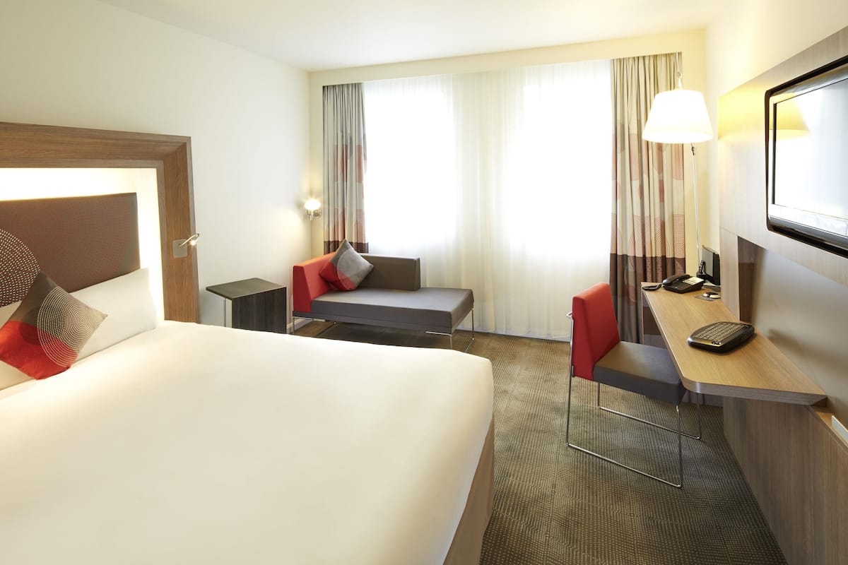 A hotel room with a bed, a desk with a telephone, a chair, a lamp, and a television.