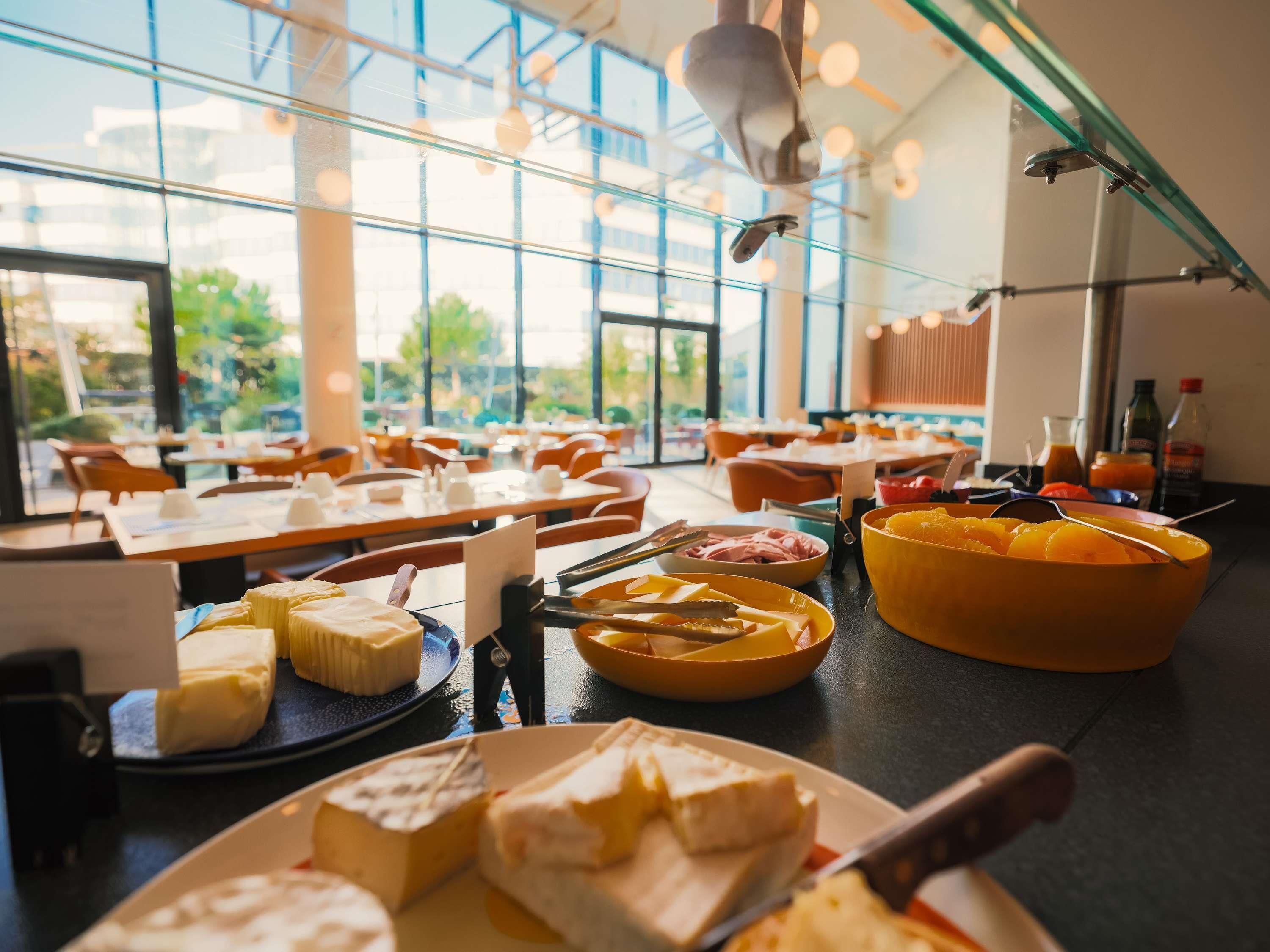 Un buffet proposant une variété de fromages et de fruits, avec des tables disposées dans une pièce spacieuse dotée de grandes fenêtres.
