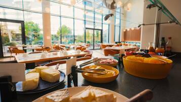 Un buffet proposant une variété de fromages et de fruits, avec des tables disposées dans une pièce spacieuse dotée de grandes fenêtres.